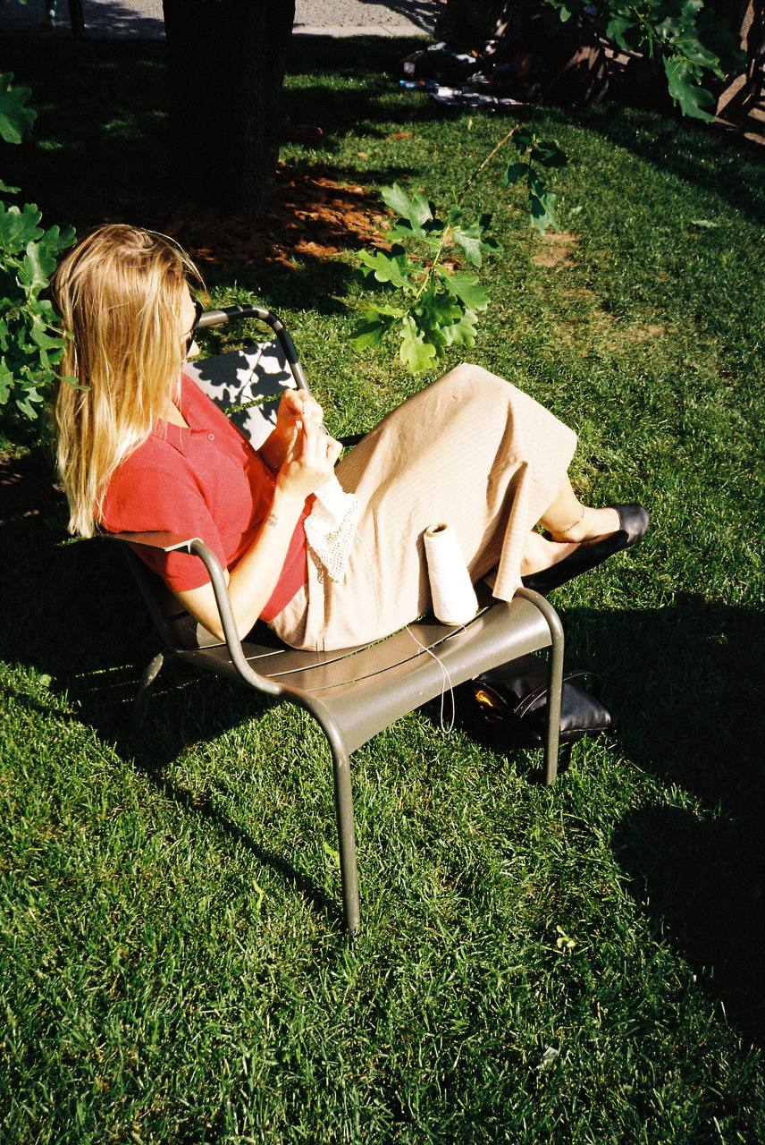 A person crocheting outdoors while sitting in a garden chair