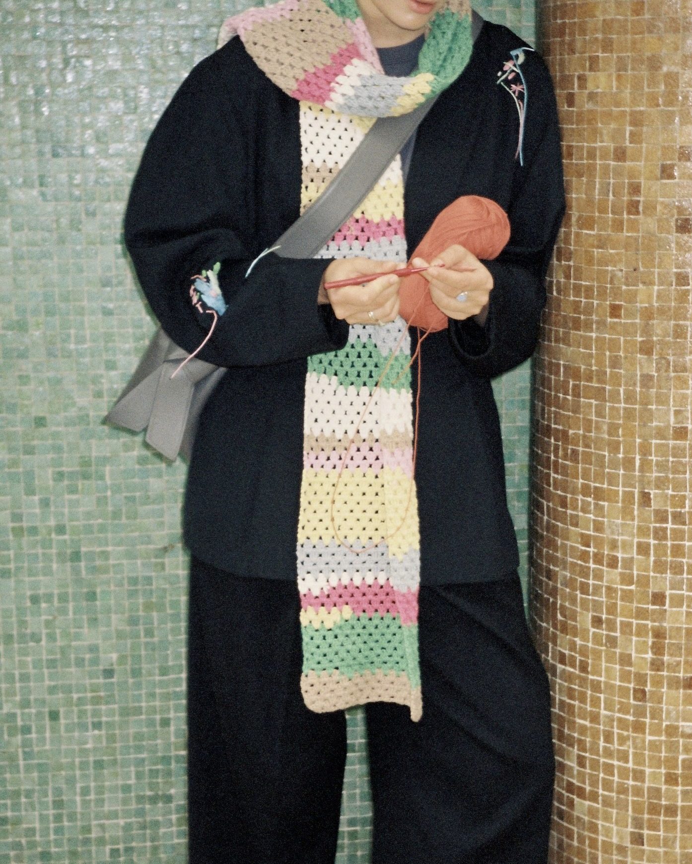 A maker crocheting while wearing a long colourful scarf